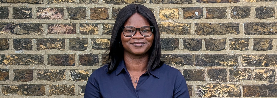 A Black woman wearing glasses looking into the camera, with a brick wall background