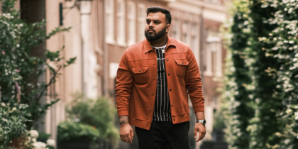 South Asian man wearing orange jacket walks along city street