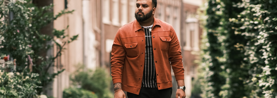 South Asian man wearing orange jacket walks along city street