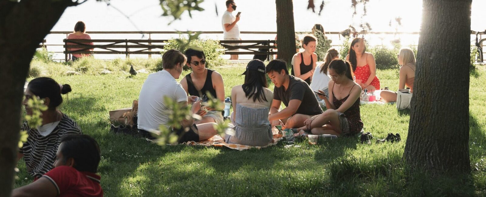 A group of people sitting under shade on a sunny day talking and eating.