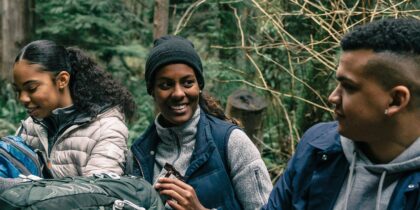 Young black man and Young black woman sat on grass, having a break from their hike, looking at each other in conversation