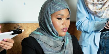 Young Black Muslim woman wearing a hijabi is working at a desk typing on her laptop.