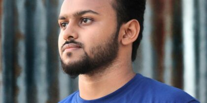 Close-up of young South Asian man with dark hair and a neatly trimmed beard, wearing a navy blue t-shirt.