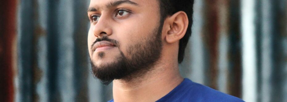 Close-up of young South Asian man with dark hair and a neatly trimmed beard, wearing a navy blue t-shirt.