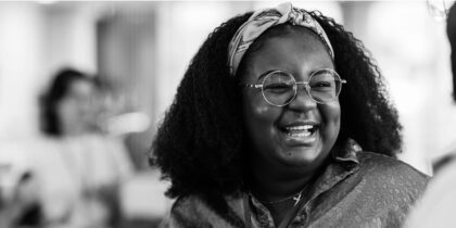 Black and white image of young Black girl smiling while in conversation with a group of people.