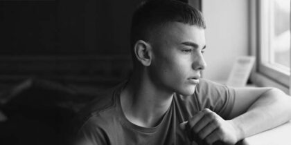 Emotional, low lighting shot of a teenage boy looking out of a window
