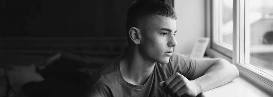 Emotional, low lighting shot of a teenage boy looking out of a window