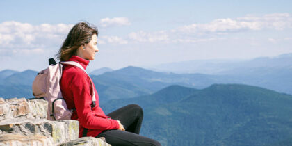 Against a background of blue sky, a woman is sitting on a mountain top admiring the view