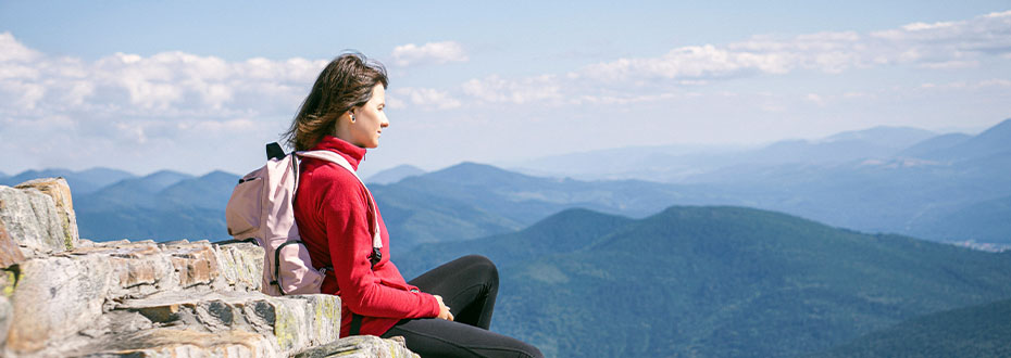 Against a background of blue sky, a woman is sitting on a mountain top admiring the view
