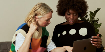Two women sitting on a sofa looking at a laptop