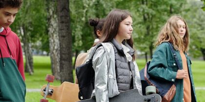 A group of children walking through a park carring skateboards