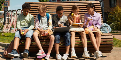 Five children sitting on a bench by a playpark in a housing development