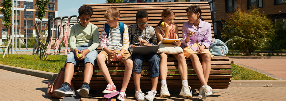 Five children sitting on a bench by a playpark in a housing development
