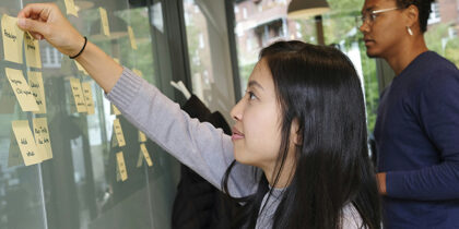 Two people are sticcking post-it notes to a wall in an office