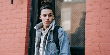 A young man stands in front of a doorway in a red brick building