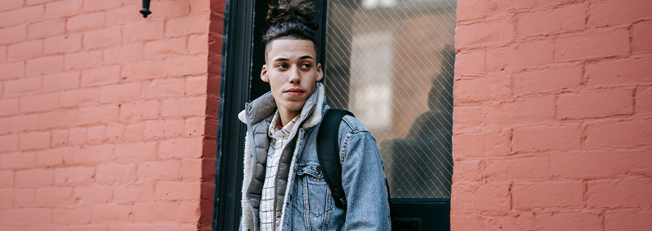 A young man stands in front of a doorway in a red brick building