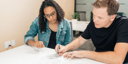 At an office desk, a woman is helping a man to fill out a form.