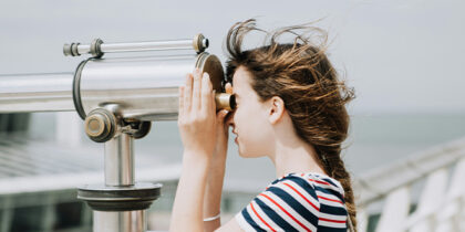 A girl is looking through a telescope at the seaside