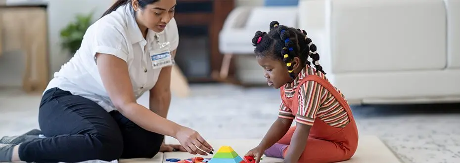 A small child and a carer sitting on the floor playing with bright bricks