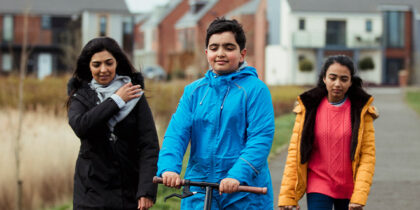 A mother and two children walking in green space with housing estate in the background