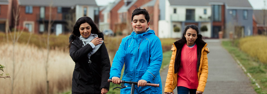 A mother and two children walking in green space with housing estate in the background