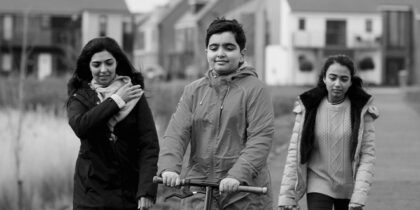 A mother and two children walking in green space with housing estate in the background