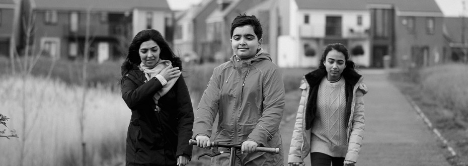 A mother and two children walking in green space with housing estate in the background