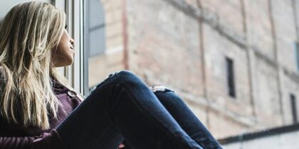 A woman sits on a windowledge looking out at buildings