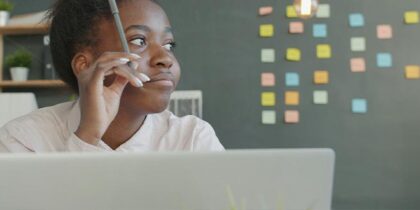 A woman in office at a laptop, looking off to the right