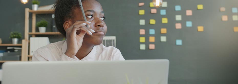 A woman in office at a laptop, looking off to the right